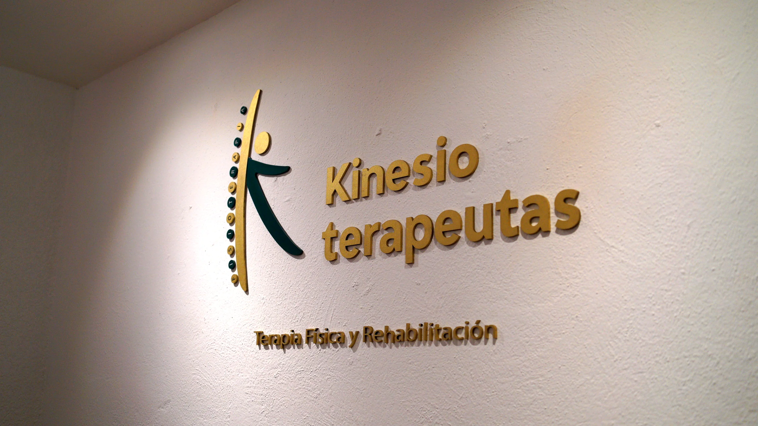 Letrero tridimensional de Kinesioterapeutas en la entrada de la clínica, con el logotipo en dorado y verde, y la leyenda Terapia Física y Rehabilitación. San Felipe del Agua, Oaxaca.